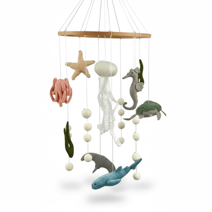 Hand-felted under-the-sea cot mobile with jellyfish, seahorse, octopus, starfish, turtle, stingray, and shark hanging from a wooden ring, 65 cm drop, on white background.